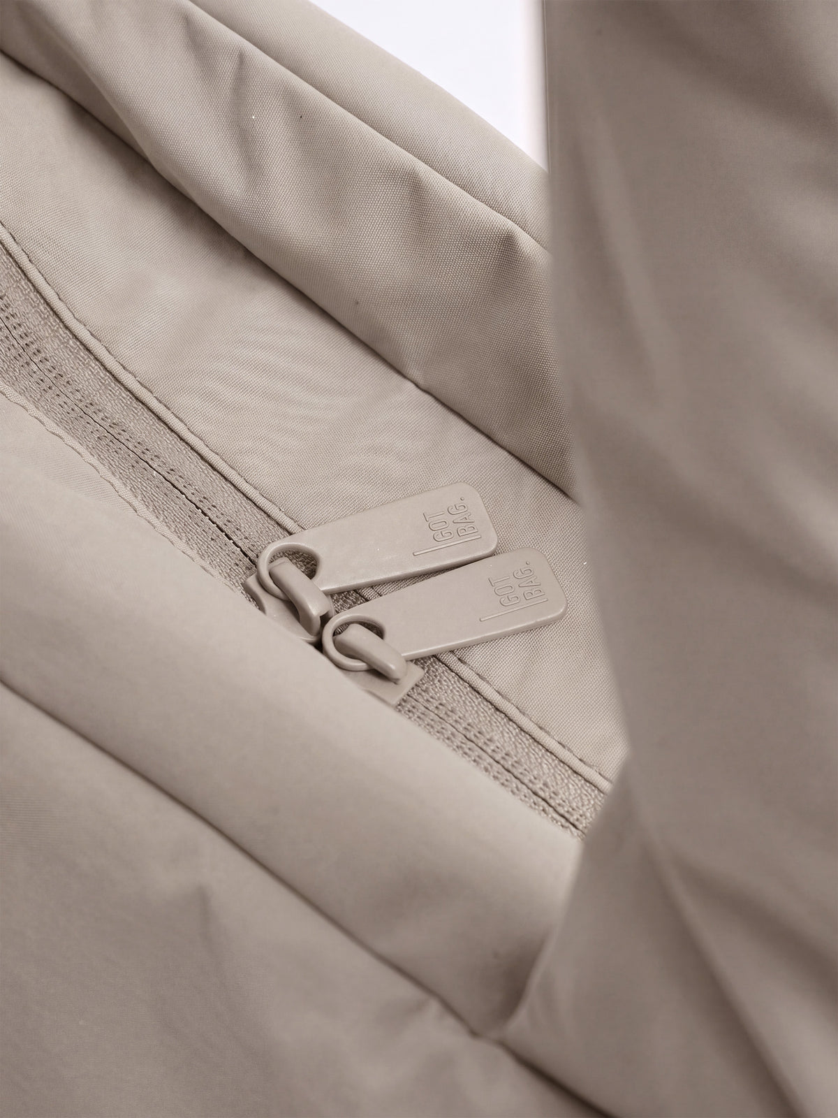 PUFFER HORIZON TOTE BAG Tasche in scallop (helles Beige) mit Detailaufnahme des Reißverschlusses und gebrandeten Zippern.