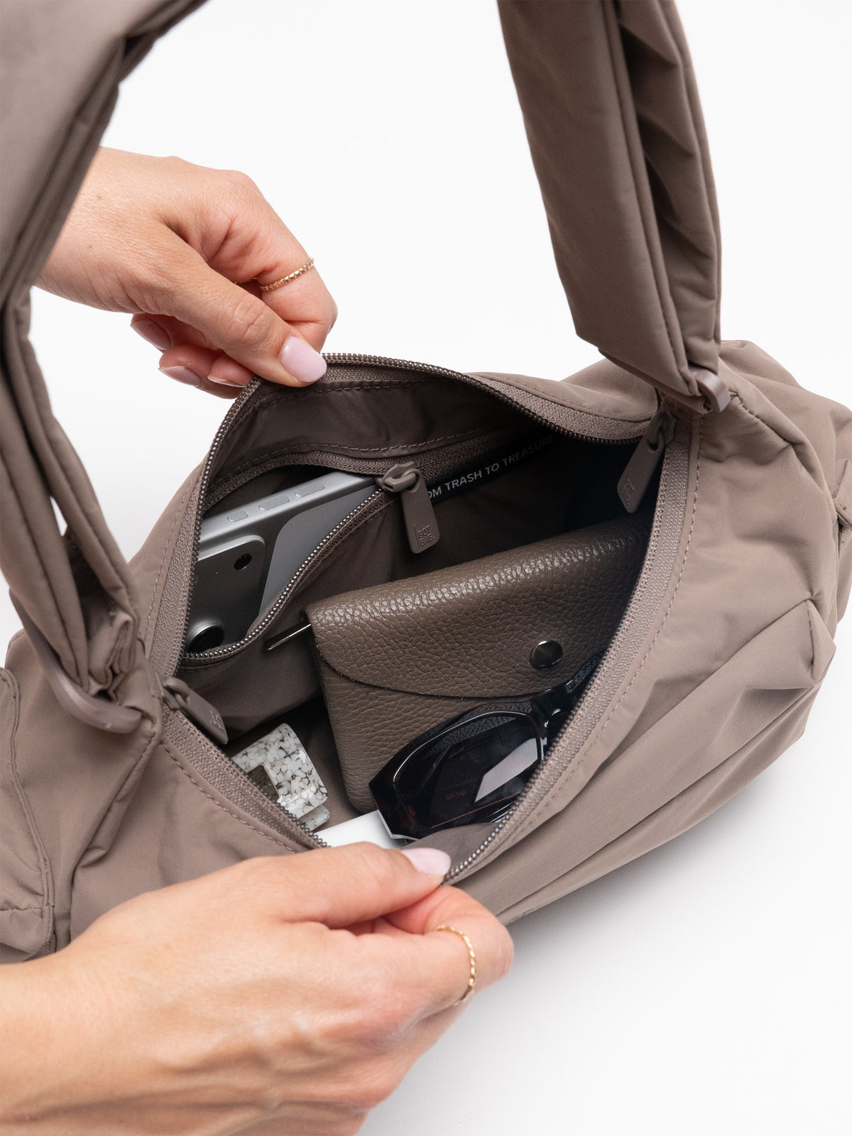 POCKET BAG SMALL Tasche in oyster (klassisches Taupe-Braun). Eine Frau öffnet den gefüllten Innenraum.
