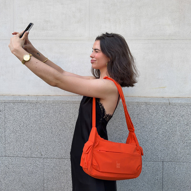 POCKET BAG SMALL bag in hot coral (vibrant orange) carried over shoulder by a woman.