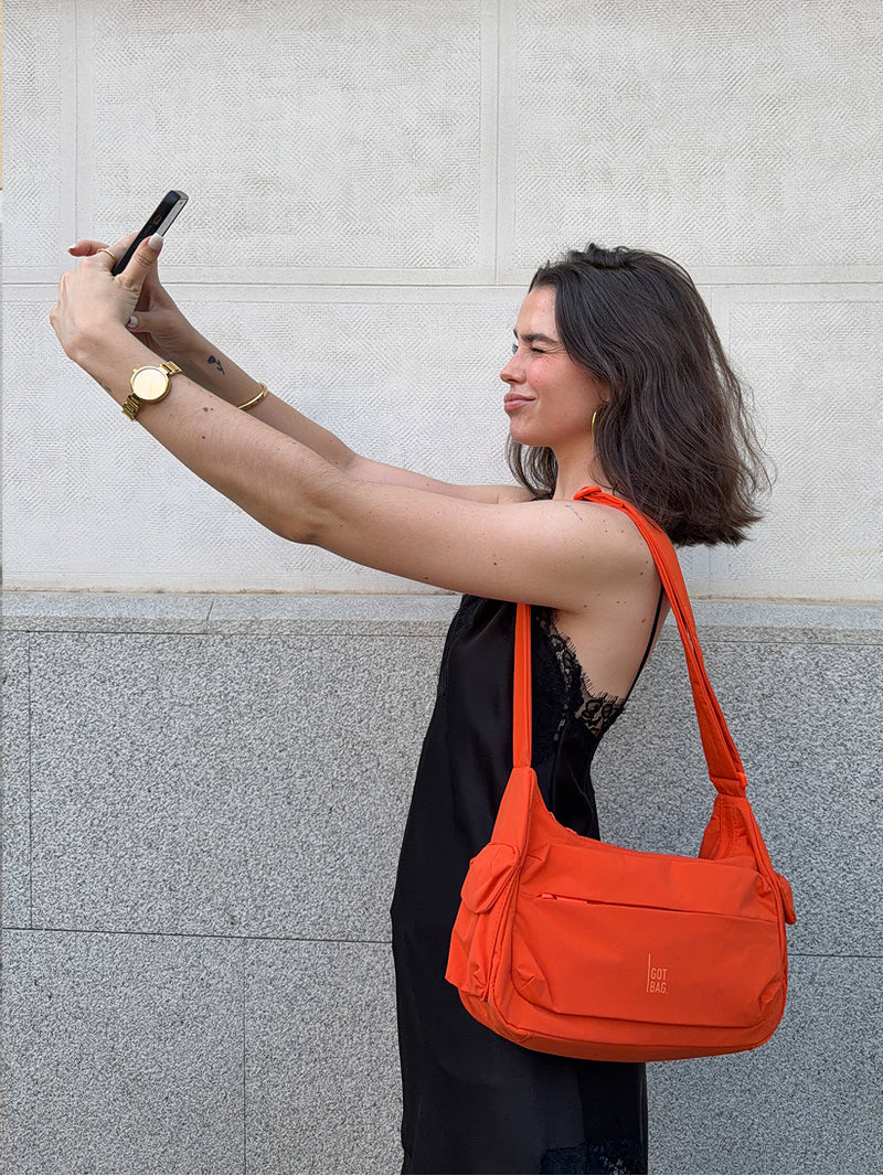 POCKET BAG SMALL bag in hot coral (vibrant orange) carried over the shoulder by a woman.