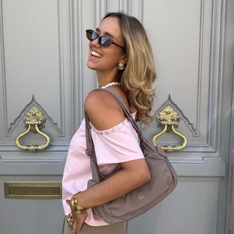 POCKET BAG SMALL bag in oyster (classic taupe-brown) carried over shoulder by a woman.