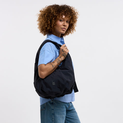 FULL MOON BAG Tasche in black (Schwarz) von einer Frau über der Schulter getragen.