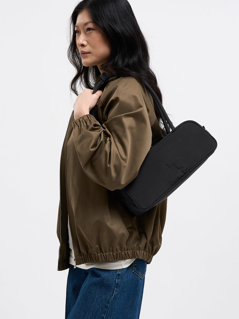 STRIKE BAG SMALL Tasche in black (Schwarz), ein Modell mit schlichter, moderner Form, von einer Frau über der Schulter getragen.