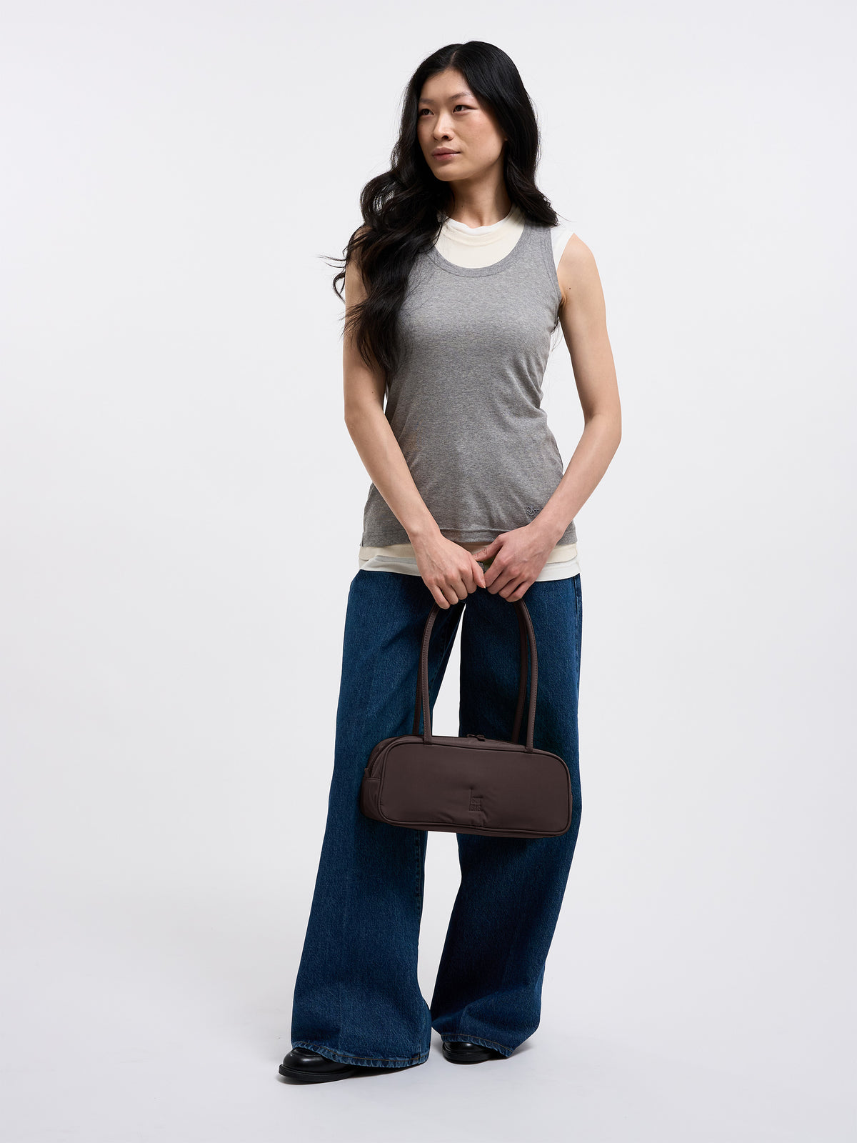 STRIKE BAG SMALL Tasche in sea lion (dunkles Schokobraun) von einer Frau in der Hand gehalten.