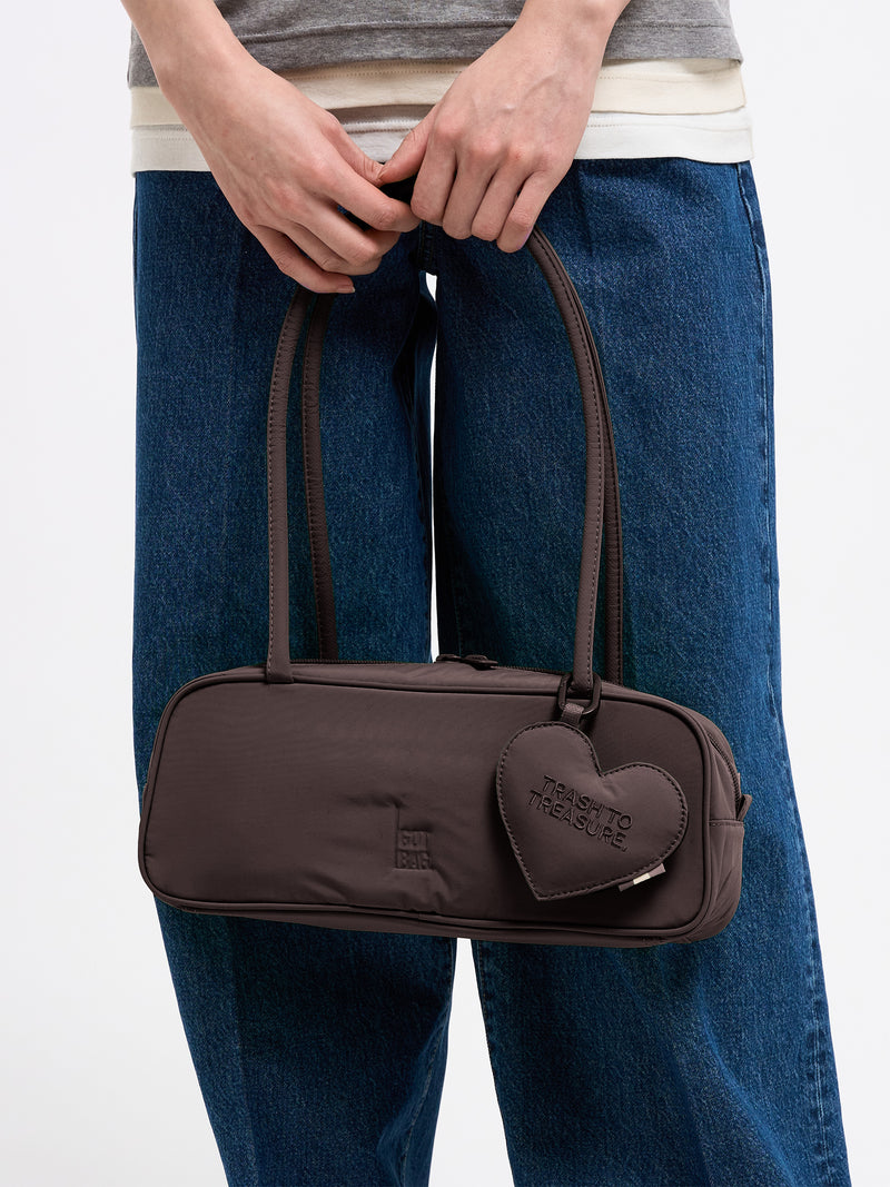 STRIKE BAG SMALL Tasche in sea lion (dunkles Schokobraun) von einer Frau in der Hand gehalten.
