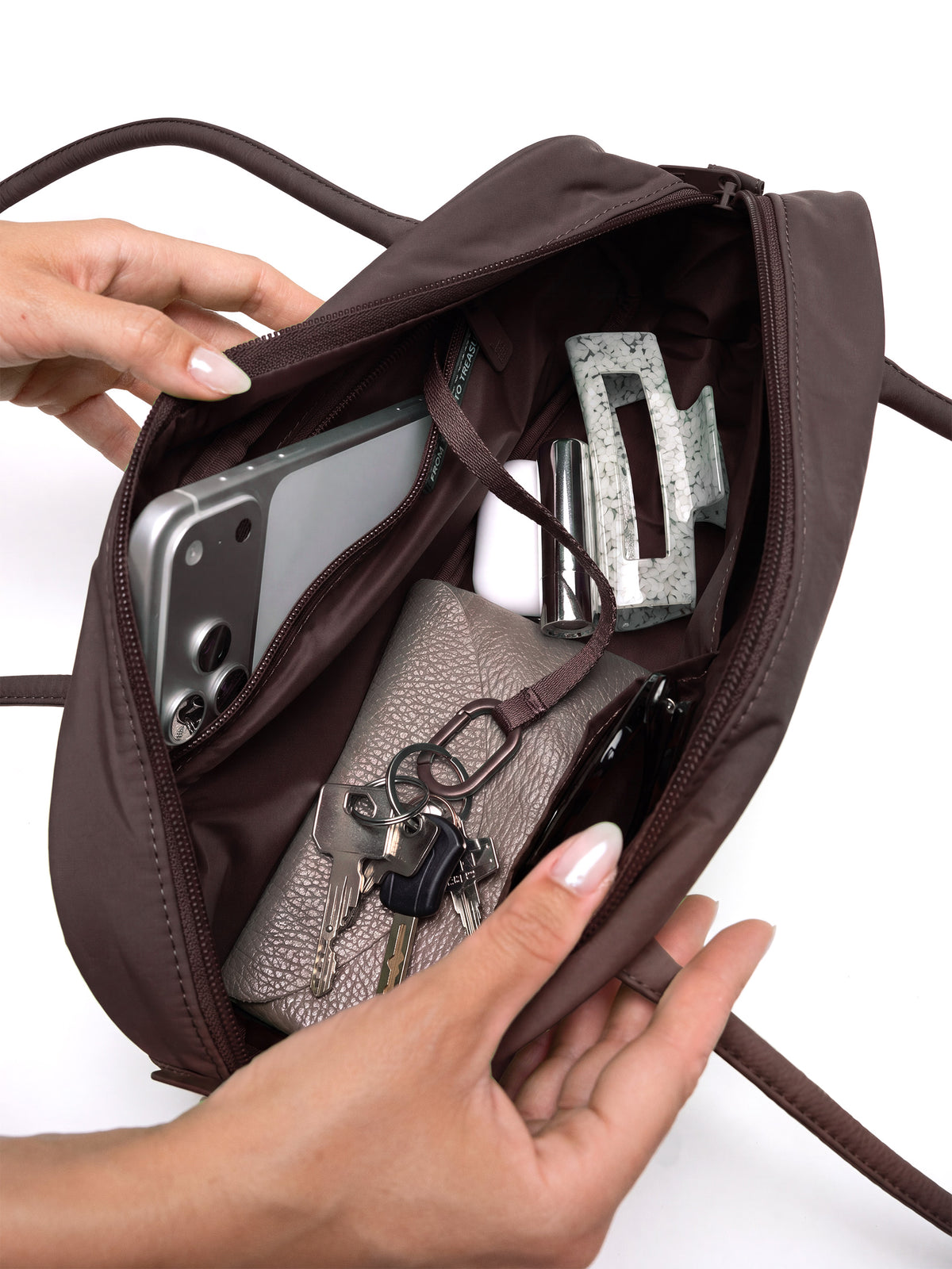 STRIKE BAG SMALL Tasche in sea lion (dunkles Schokobraun) von einer Frau geöffnet und von innen gefüllt gezeigt.