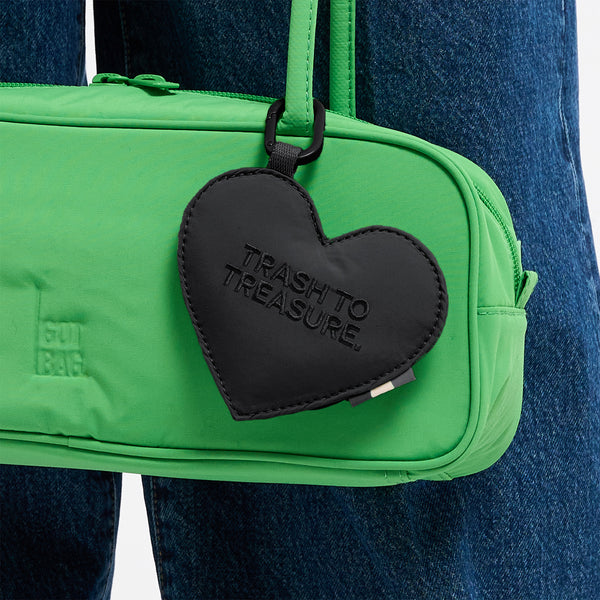 STRIKE BAG SMALL Tasche von einer Person über der Hüfte getragen, mit herzförmigem TRASH TO TREASURE Anhänger.
