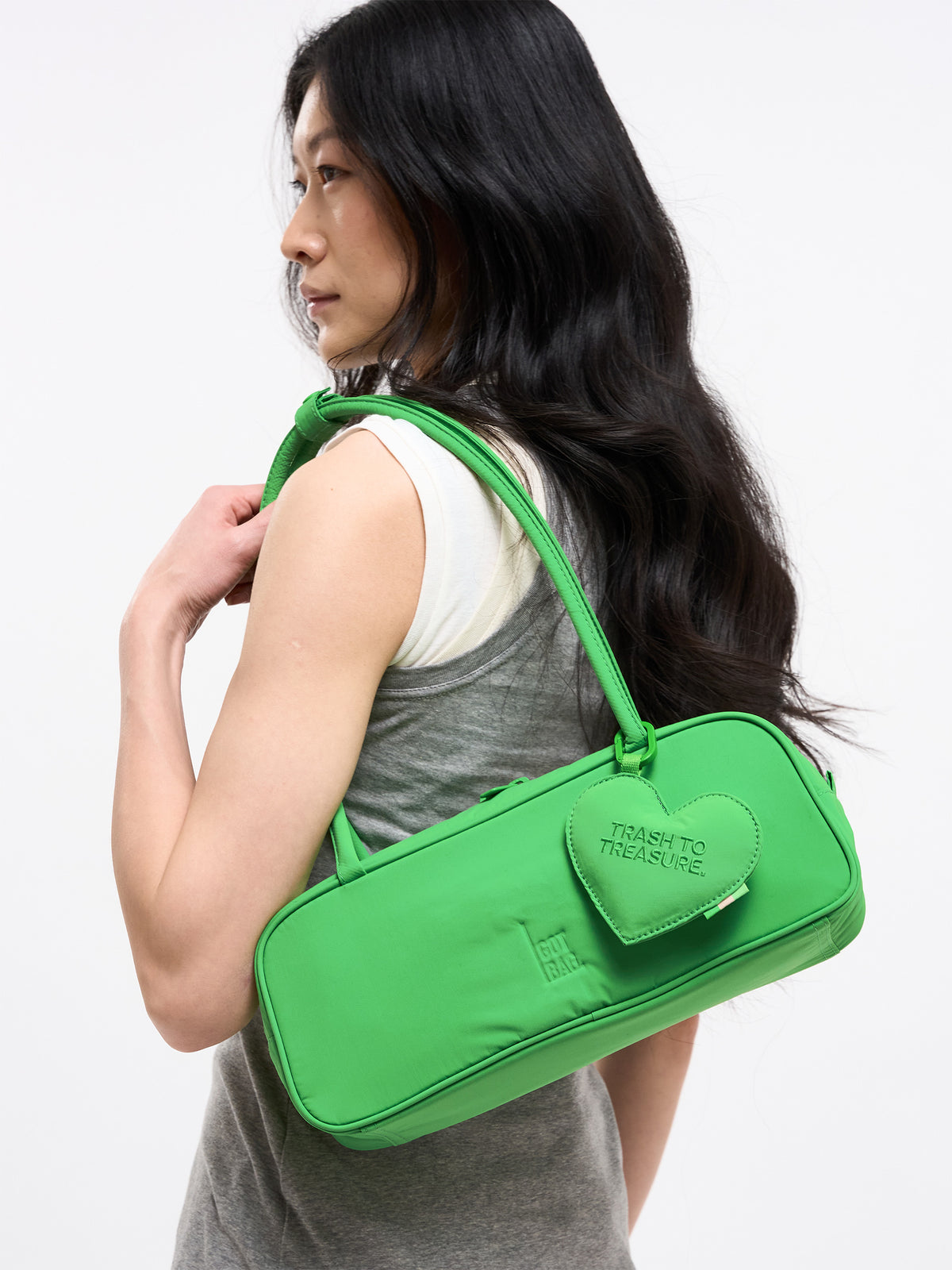 STRIKE BAG SMALL Tasche in leaf von einer Frau über der Schulter getragen, mit TRASH TO TREASURE Herzanhänger.
