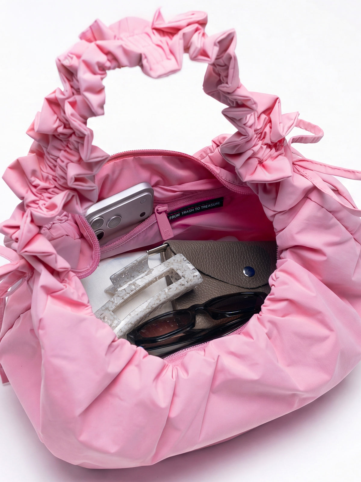 MOON BAG BOW Tasche in sea rose (sattes Pastell-Rosa), offen mit Inhalt (Handy, Sonnenbrille, Haarklammern).