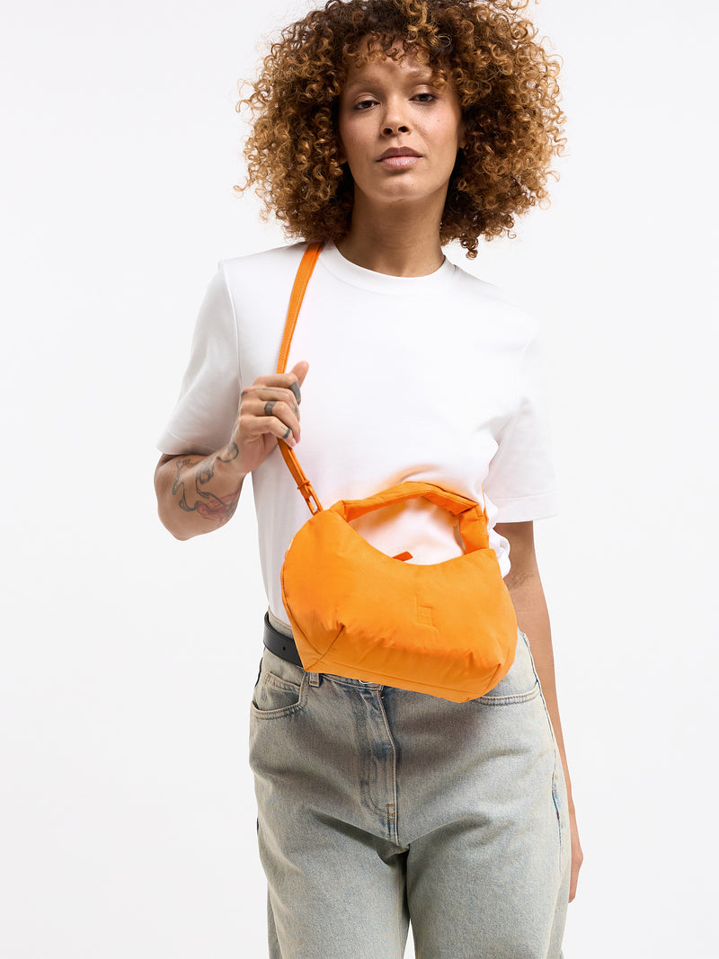 CLOUD BEAD BAG Tasche in clownfish (leuchtendes Orange-Gelb) von einer Frau in der Hand gehalten.