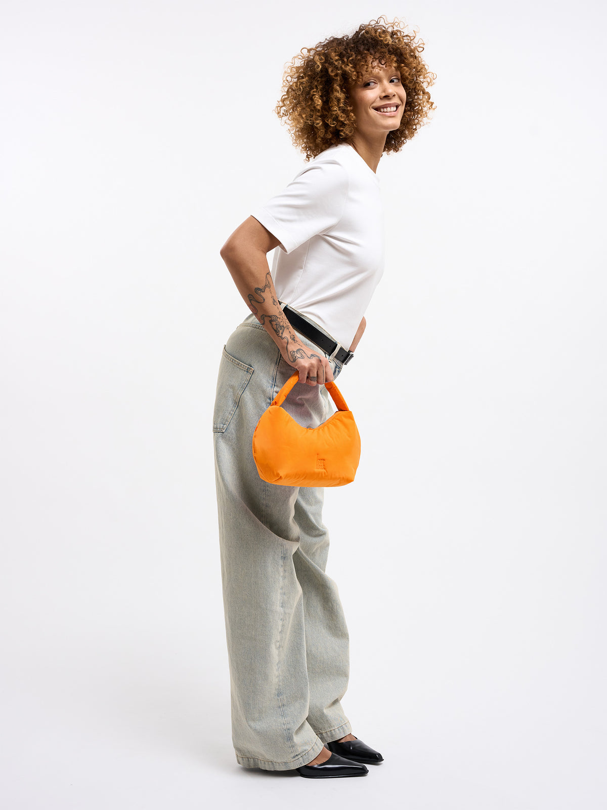CLOUD BEAD BAG Tasche in clownfish (leuchtendes Orange-Gelb) von einer Frau in der Hand gehalten.