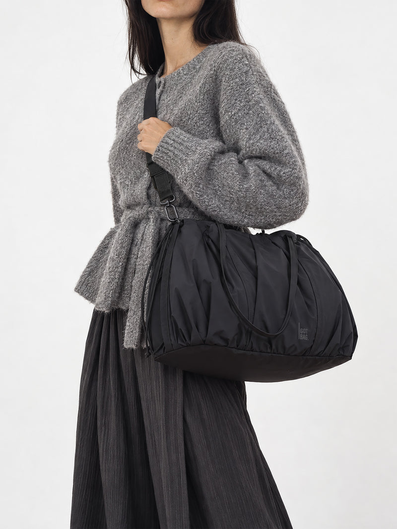 SHELLY TOTE BAG Tasche in black (Schwarz) von einer Frau über der Schulter getragen.