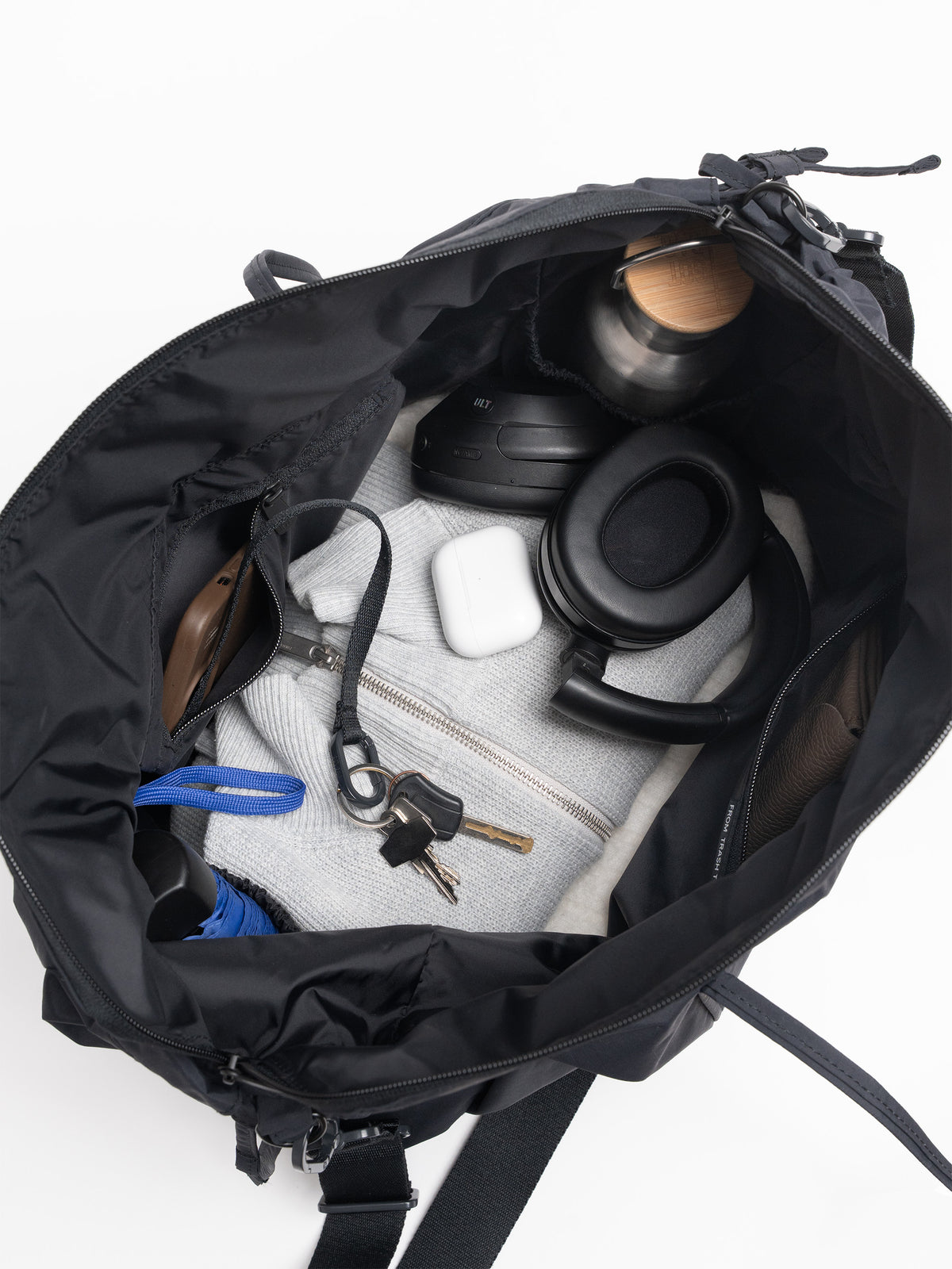 SHELLY TOTE BAG Tasche in black (Schwarz) von oben, gefüllt mit Kopfhörern, Schlüsseln und Trinkflasche.