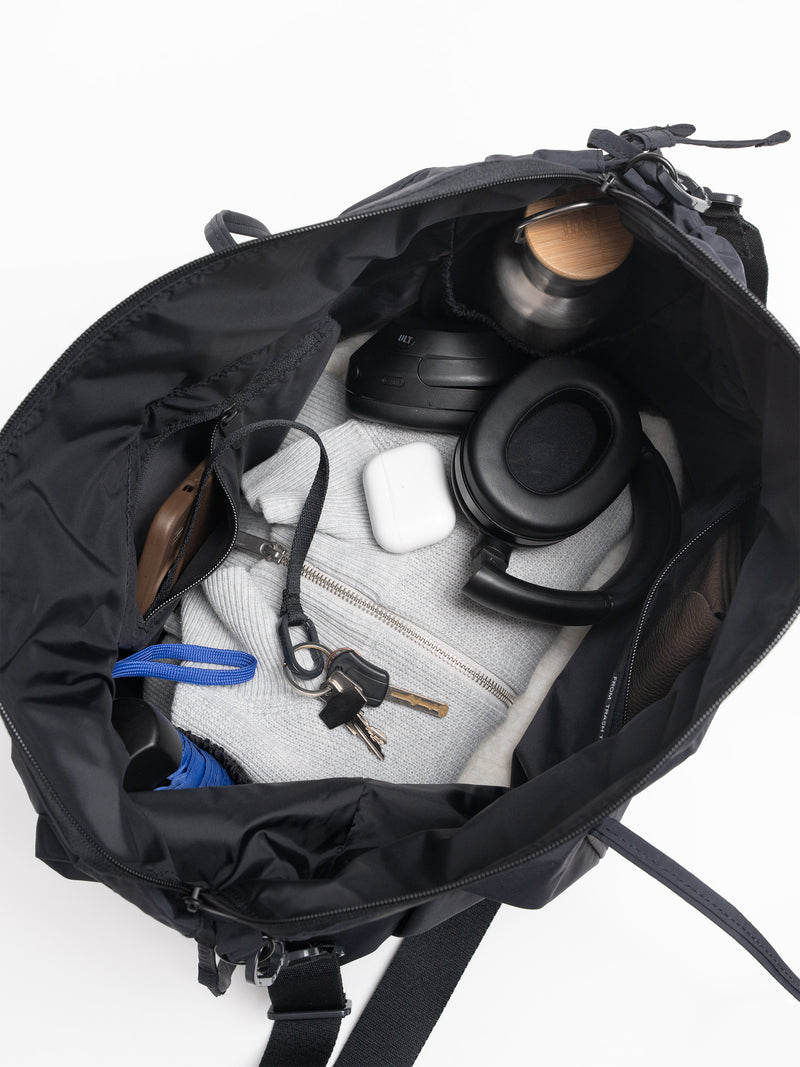 SHELLY TOTE BAG Tasche in black (Schwarz) von oben, gefüllt mit Kopfhörern, Schlüsseln und Trinkflasche.
