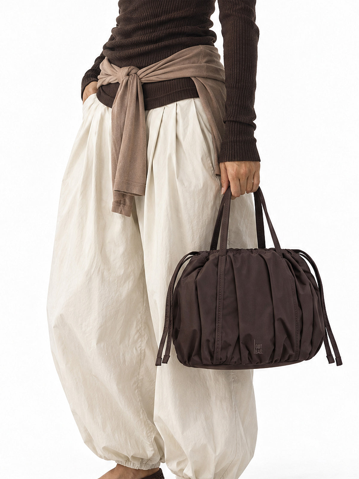 SHELLY BUCKET BAG Tasche in sea lion (dunkles Schokobraun) von einer Frau in der Hand gehalten.