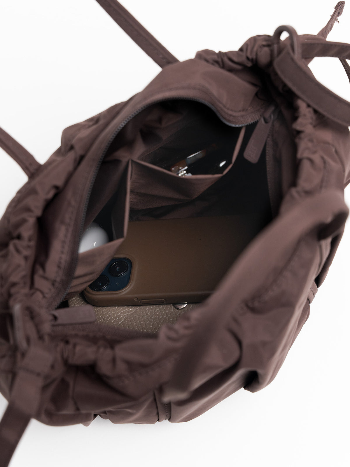 SHELLY BUCKET BAG Tasche in sea lion (dunkles Schokobraun) mit Smartphone und Schlüssel im Inneren.