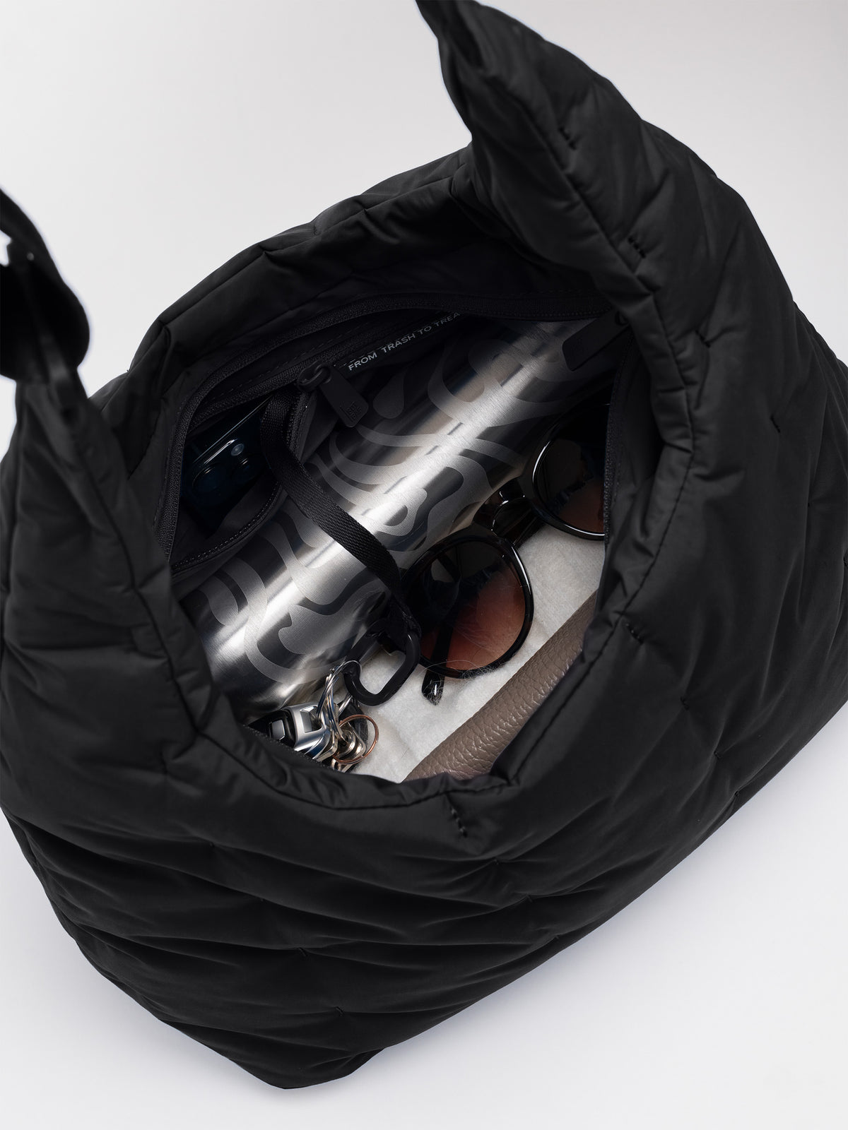 LOOMI SHOULDER BAG Tasche in black (Schwarz) als Detailaufnahme vom Inneren, gefüllt mit Wasserflasche, Sonnenbrille und Schlüsseln.