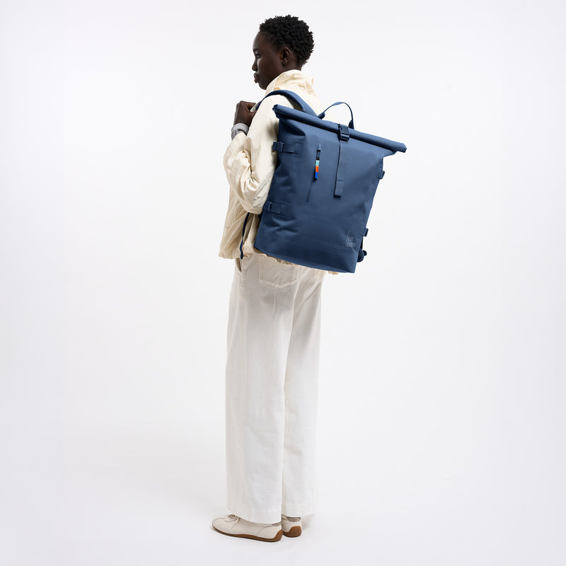 ROLLTOP Rucksack in ocean blue (Marineblau) von einer Frau auf dem Rücken getragen.