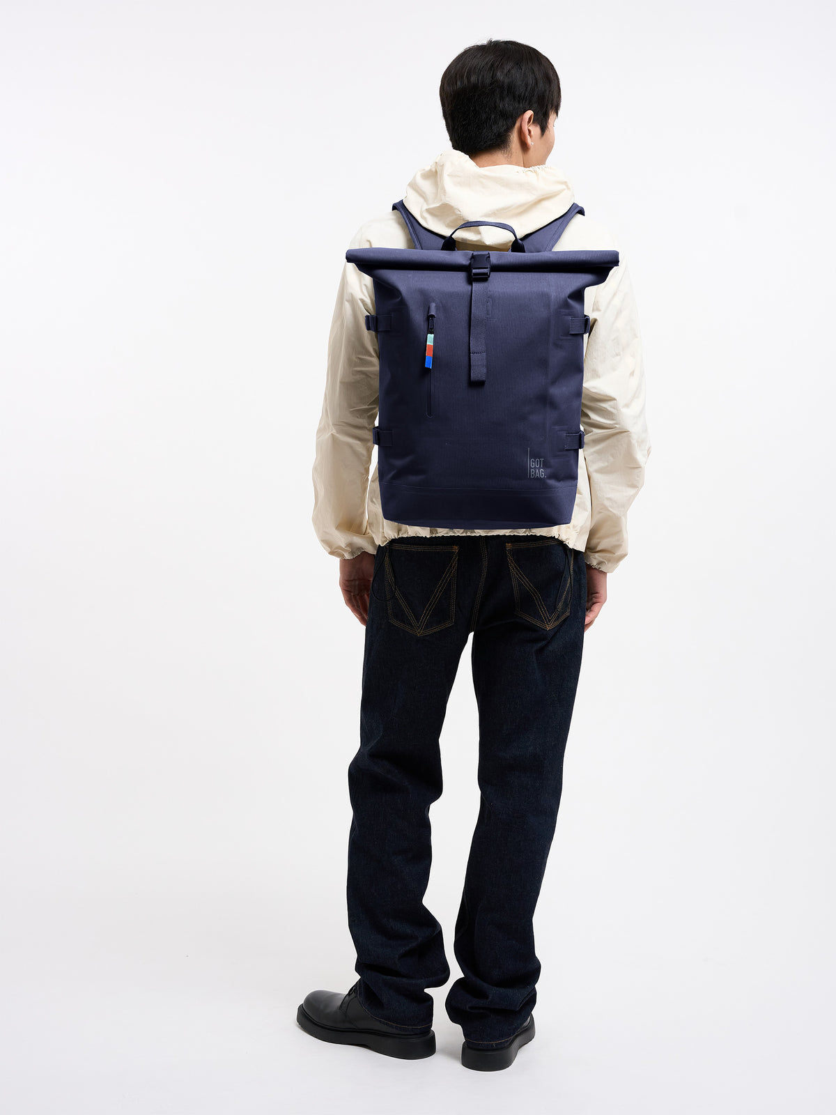 ROLLTOP Rucksack in tide (tiefes Dunkelblau mit Lilastich) von einem Mann auf dem Rücken getragen.