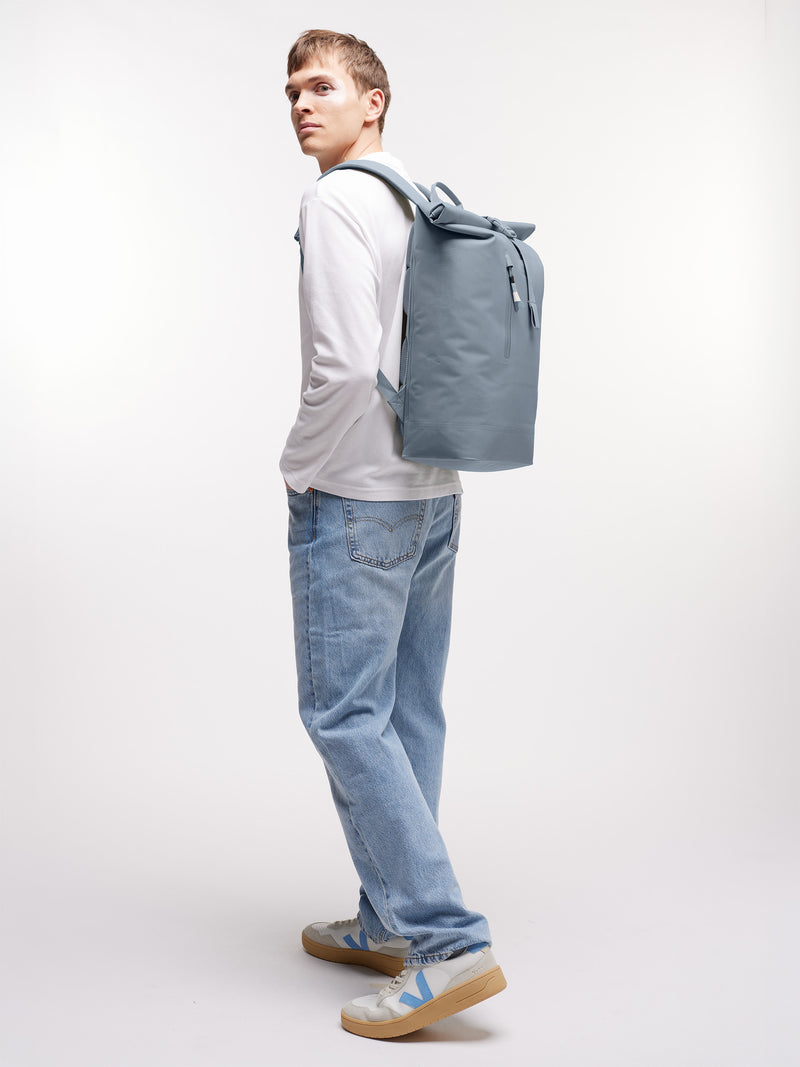 ROLLTOP LITE MONOCHROME Rucksack in marlin (grau-blau) von einem Mann auf dem Rücken getragen.