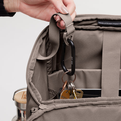 PRO PACK MONOCHROME Rucksack in oyster (klassisches Taupe-Braun). Detailaufnahme des geöffneten Innenraums mit Karabiner und Schlüsseln, von einer Hand gehalten.