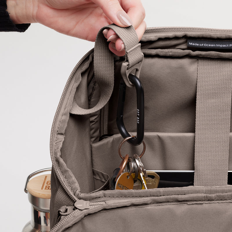 PRO PACK MONOCHROME Rucksack in oyster (klassisches Taupe-Braun). Detailaufnahme des geöffneten Innenraums mit Karabiner und Schlüsseln, von einer Hand gehalten.