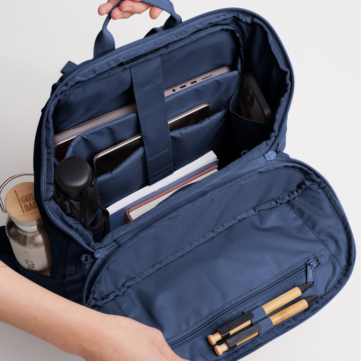 BP0083MO PRO PACK MONOCHROME Rucksack in deep ocean (dunkles Marineblau) mit geöffnetem Hauptfach, gefüllt mit Laptop, Tablet, Flasche & Büchern.