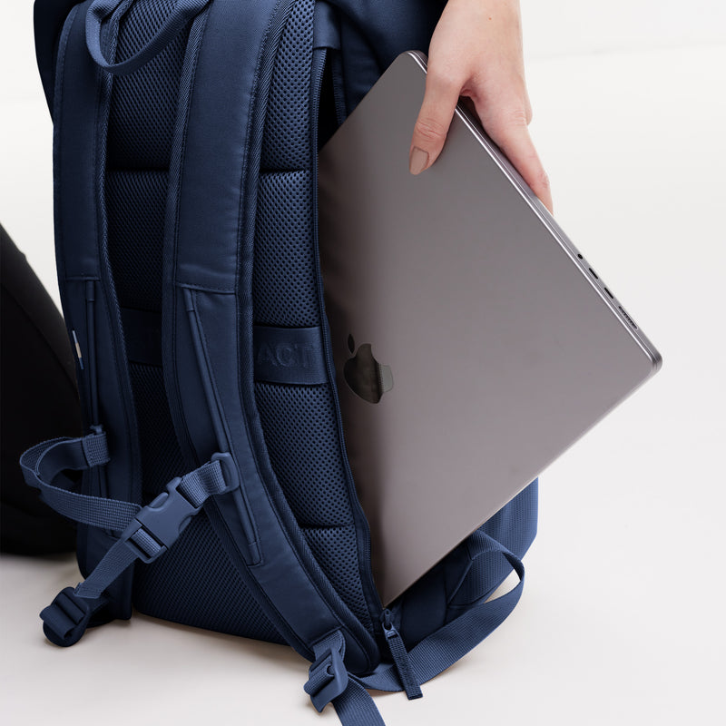 PRO PACK MONOCHROME Rucksack in deep ocean (dunkles Marineblau), eine Hand steckt einen Laptop in die Rückentasche.