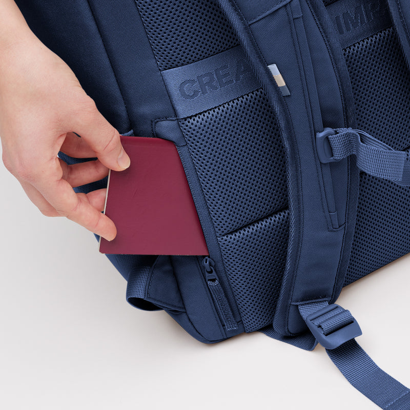 PRO PACK MONOCHROME Rucksack in deep ocean (dunkles Marineblau) mit einer Hand, die einen Pass in eine Geheimtasche steckt.