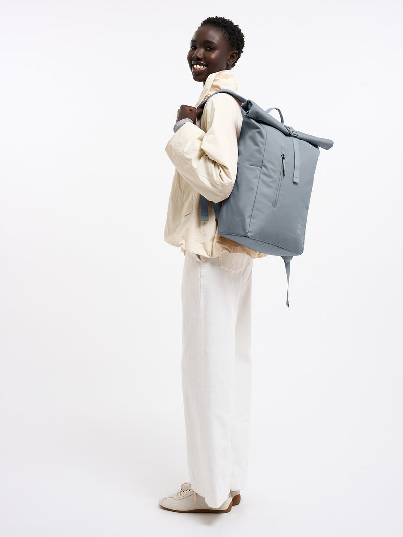 ROLLTOP EASY MONOCHROME Rucksack in marlin (grau-blau) von einer Frau als Rucksack auf dem Rücken getragen.