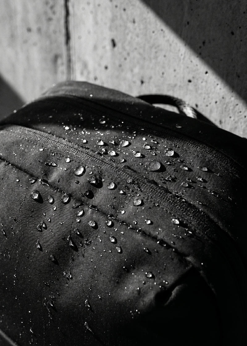 COMMUTER PACK zaino in black (nero), primo piano con gocce d'acqua su superficie resistente all'acqua.