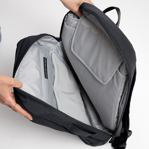COMMUTER PACK Rucksack in shark (Dunkelgrau), von Händen geöffnet, zeigt Innenfächer und Etikett.