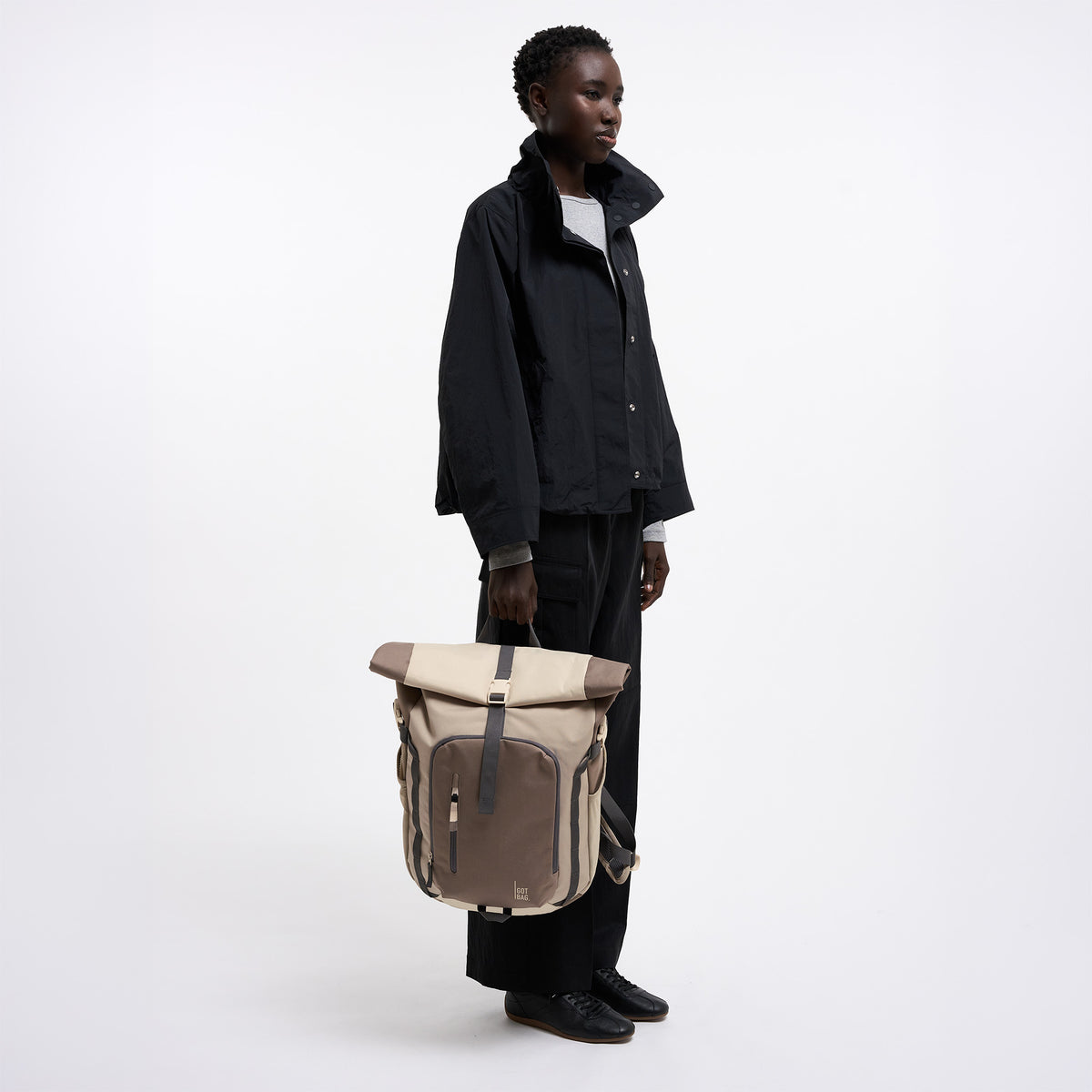 ROLLTOP ADVENTURE MONOCHROME Rucksack in oyster (klassisches Taupe-Braun) von einer Frau in der Hand gehalten.
