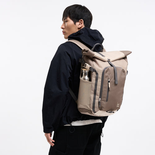 ROLLTOP ADVENTURE MONOCHROME Rucksack in oyster (klassisches Taupe-Braun) von einem Mann auf dem Rücken getragen.