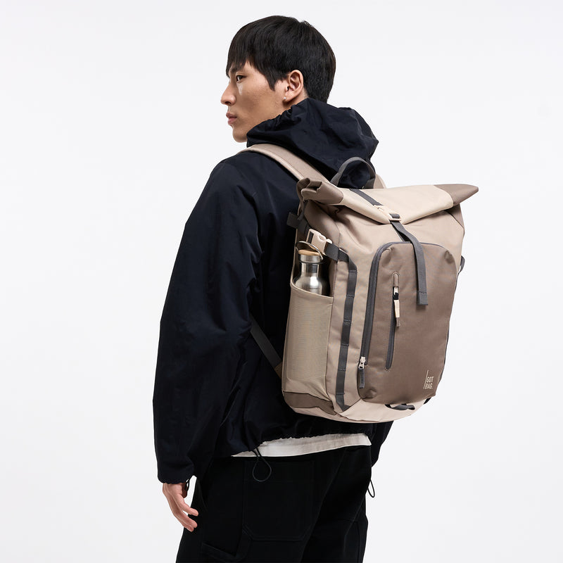 ROLLTOP ADVENTURE MONOCHROME Rucksack in oyster (klassisches Taupe-Braun) von einem Mann auf dem Rücken getragen.