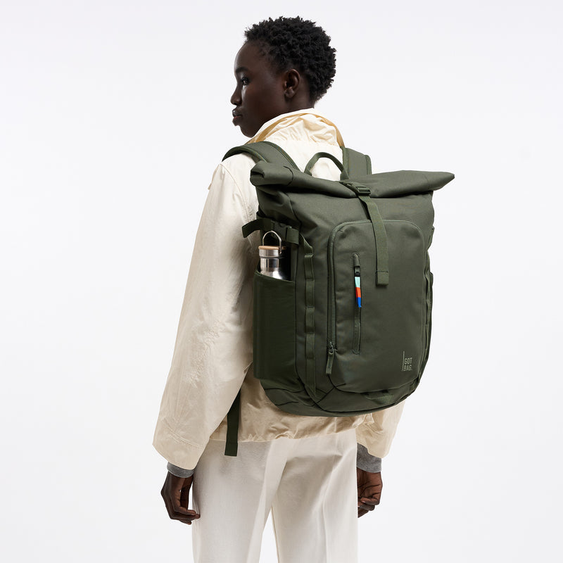 ROLLTOP ADVENTURE Rucksack in algae (Dunkelgrün mit Graustich) von einer Frau auf dem Rücken getragen, mit Trinkflasche.