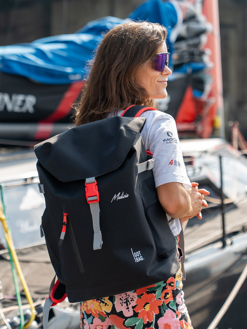 MALIZIA PACK Rucksack in black (Schwarz) von einer Frau im Freien als Rucksack auf dem Rücken getragen.
