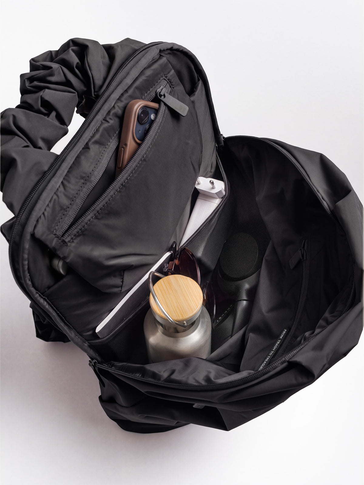 RUFFLE PACK Rucksack in black (Schwarz) mit offenem Innenraum, gefüllt mit Alltagsgegenständen.
