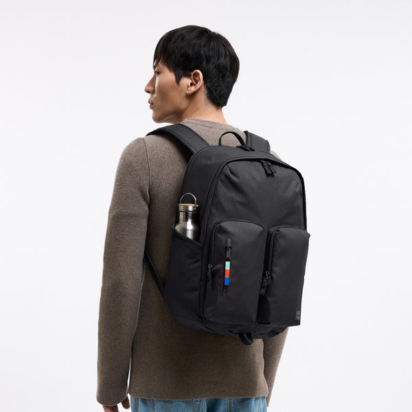 BASE PACK Rucksack in black (Schwarz), von einem Mann auf dem Rücken getragen.