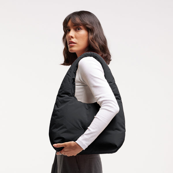 CLOUD SHOULDER BAG Tasche in black (Schwarz) von einer Frau über der Schulter getragen.