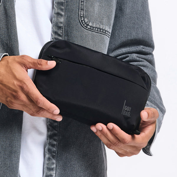 COMMUTER TECH POUCH Tasche in black (Schwarz) von einem Mann in der Hand gehalten.