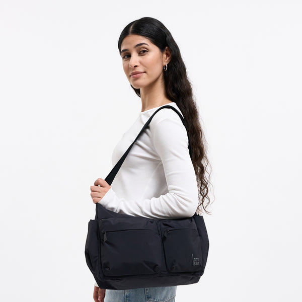 POCKET SLING BAG Tasche in black (Schwarz) von einer Frau über der Schulter getragen.