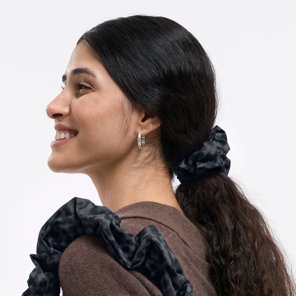 Eine Frau trägt ein Scrunchie Accessoire in black (Schwarz) im Haar, lächelnd im Profil.