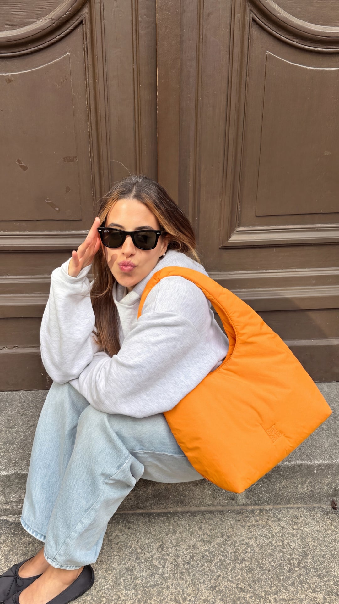 CLOUD SHOULDER BAG Tasche in clownfish (leuchtendes Orange-Gelb) von einer Frau über der Schulter getragen.