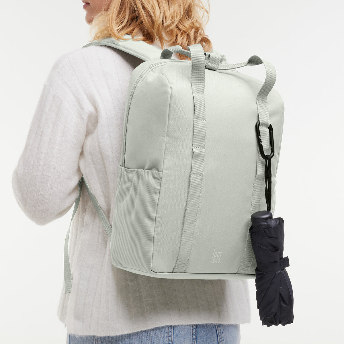 DAYPACK LOOP Rucksack in eel (sehr helles Grün/Mint) von einer Frau auf dem Rücken getragen, mit schwarzem Regenschirm.