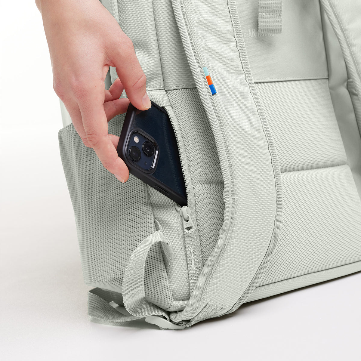 DAYPACK LOOP Rucksack in eel (sehr helles Grün/Mint), Detailaufnahme einer Hand, die ein Smartphone in die Seitentasche steckt.