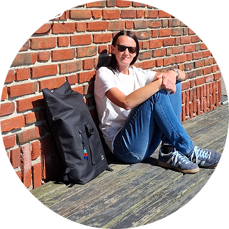 Backpack next to a woman sitting on wooden floor in front of a brick wall.