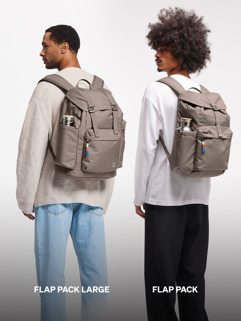 FLAP PACK LARGE Rucksack in oyster (klassisches Taupe-Braun) von zwei Männern auf dem Rücken getragen.