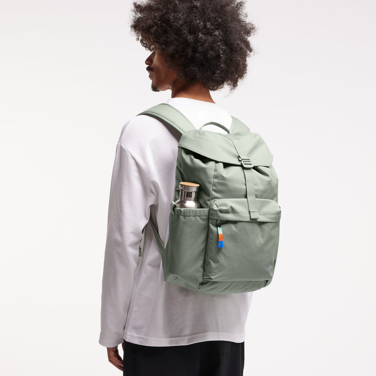 FLAP PACK Rucksack in bass (Salbeigrün) von einem Mann auf dem Rücken getragen.