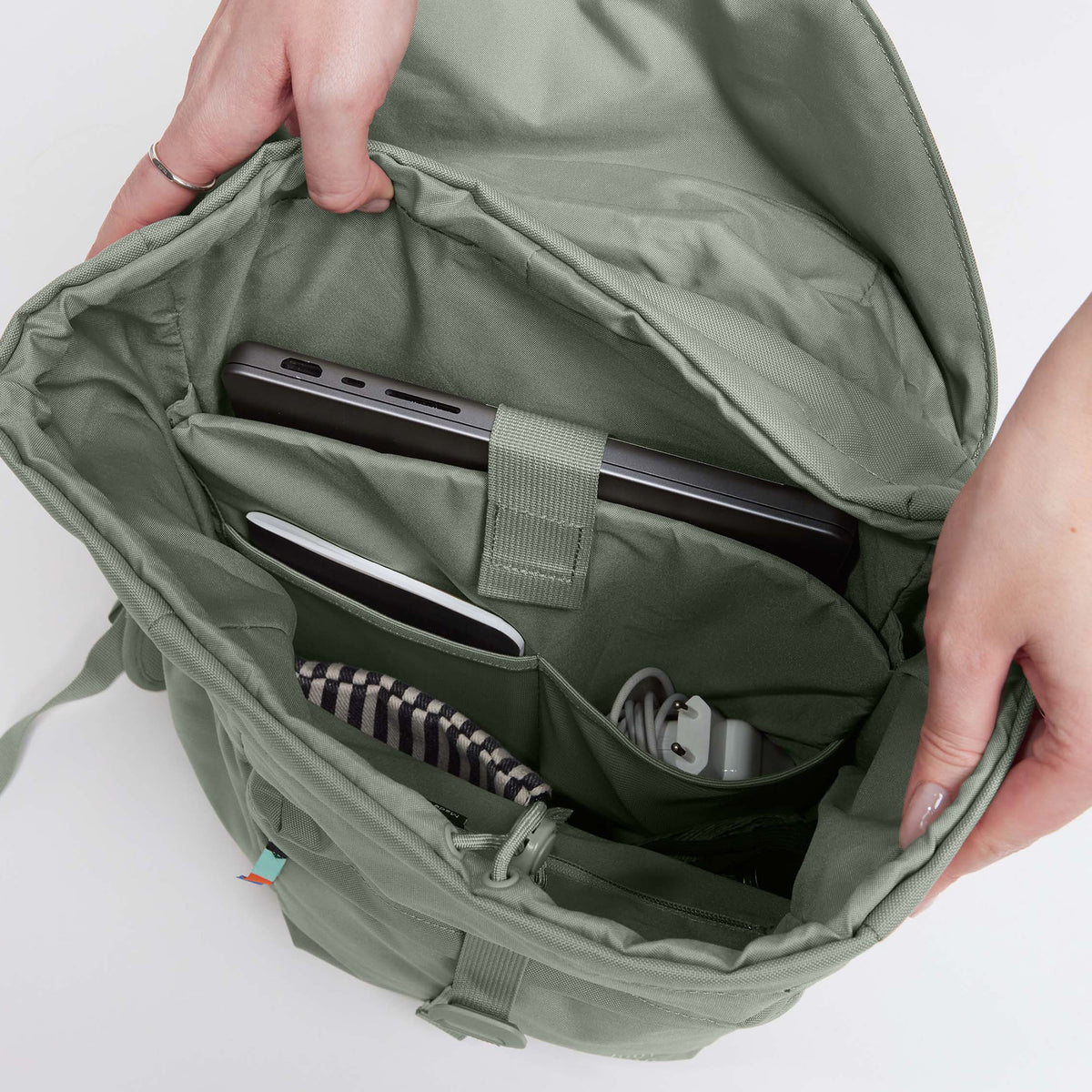 FLAP PACK Rucksack in bass (Salbeigrün), von einer Frau geöffnet, zeigt Laptop und Zubehör.